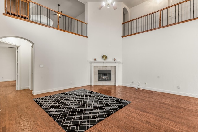 unfurnished living room with wood finished floors, a fireplace, a high ceiling, arched walkways, and a ceiling fan