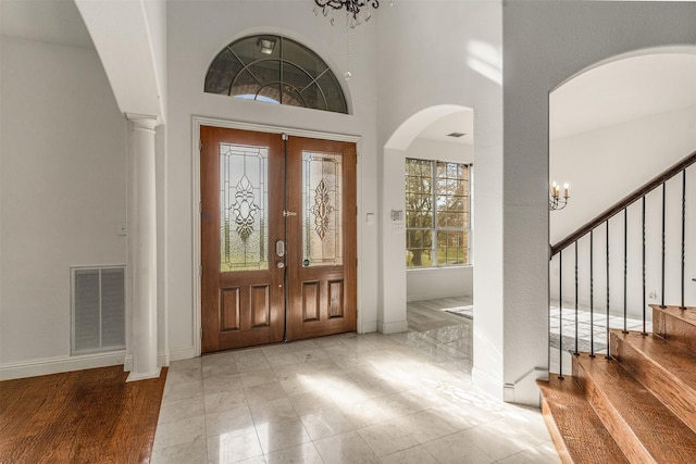 foyer entrance with visible vents, baseboards, french doors, arched walkways, and a notable chandelier