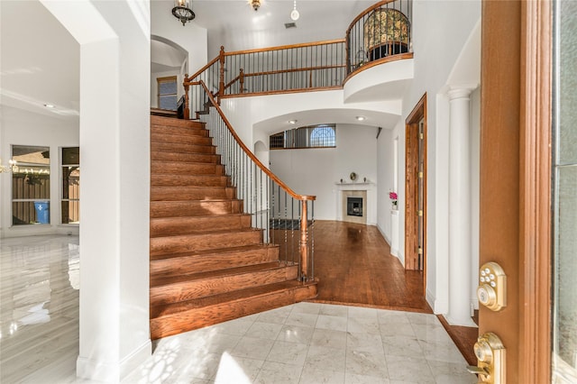 entrance foyer with a towering ceiling, a fireplace, stairs, and marble finish floor