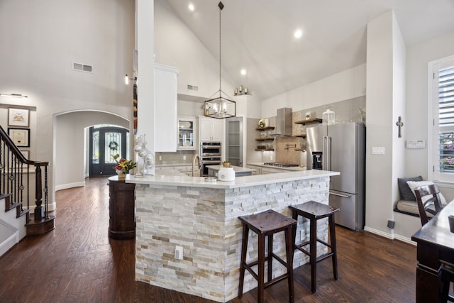 2937 Lago Vista Ln, Rockwall, TX 75032 - kitchen featuring appliances with stainless steel finishes, arched walkways, dark wood-type flooring, a peninsula, and high vaulted ceiling