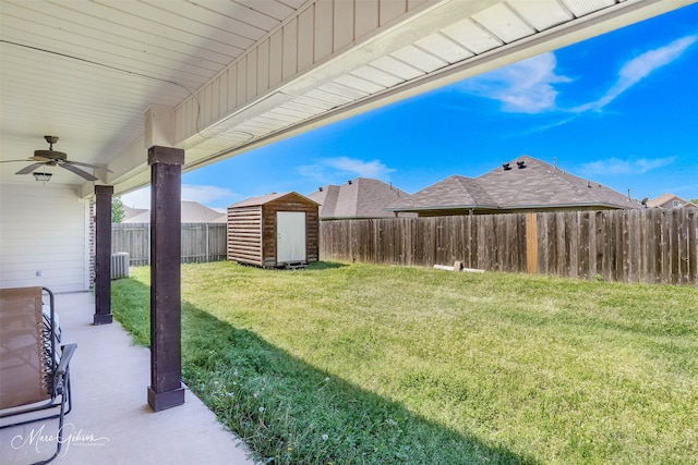 view of yard featuring a shed, a fenced backyard, a ceiling fan, and an outbuilding