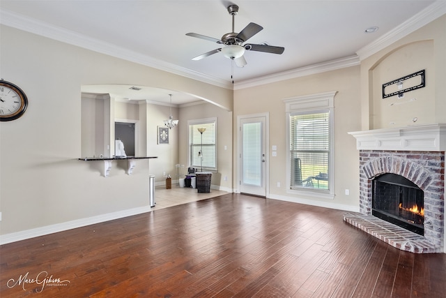 unfurnished living room with crown molding, a ceiling fan, wood finished floors, a brick fireplace, and baseboards