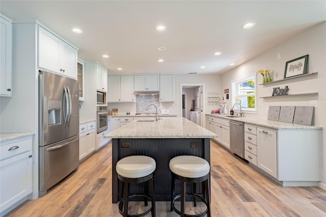 kitchen featuring a sink, appliances with stainless steel finishes, light wood-style floors, and an island with sink