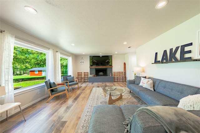 living area featuring recessed lighting, light wood finished floors, a fireplace with raised hearth, and baseboards