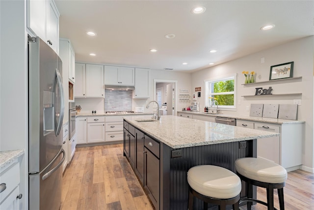 kitchen with tasteful backsplash, a sink, light wood-type flooring, appliances with stainless steel finishes, and white cabinetry