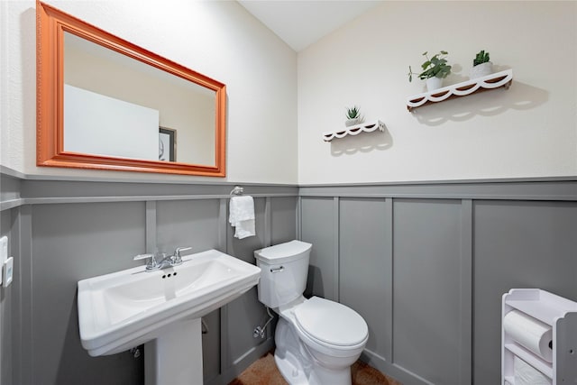 half bath featuring toilet, a decorative wall, a sink, and a wainscoted wall