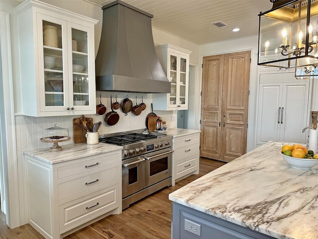 712 Camp Cypress Trl, Winnsboro, TX 75494 - kitchen with white cabinets, a chandelier, wood finished floors, wall chimney exhaust hood, and range with two ovens