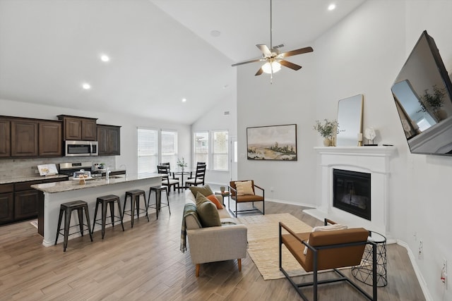 living area featuring light wood-type flooring, high vaulted ceiling, a glass covered fireplace, and recessed lighting