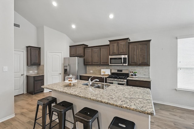 kitchen featuring vaulted ceiling, visible vents, a kitchen bar, stainless steel appliances, and a sink