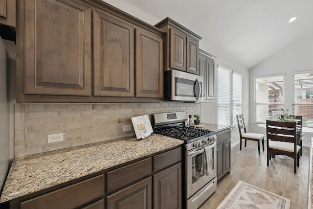 kitchen featuring light wood-style floors, appliances with stainless steel finishes, lofted ceiling, baseboards, and backsplash