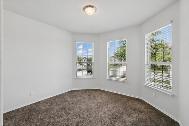 unfurnished room with dark colored carpet, baseboards, and plenty of natural light