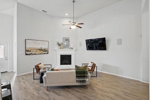 living area with wood finished floors, baseboards, a glass covered fireplace, and visible vents