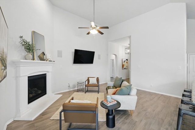 living area featuring a glass covered fireplace, arched walkways, ceiling fan, and wood finished floors