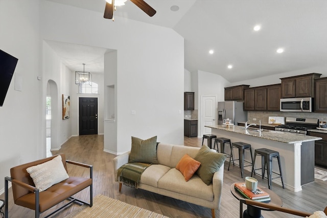 living area featuring recessed lighting, light wood-style flooring, high vaulted ceiling, arched walkways, and ceiling fan with notable chandelier