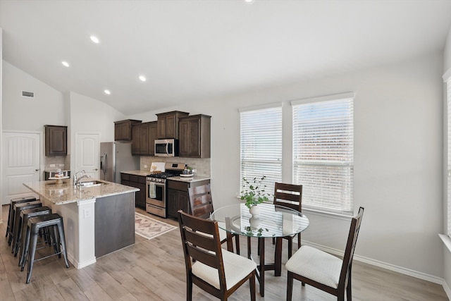 kitchen with appliances with stainless steel finishes, dark brown cabinetry, light wood-style floors, decorative backsplash, and a sink