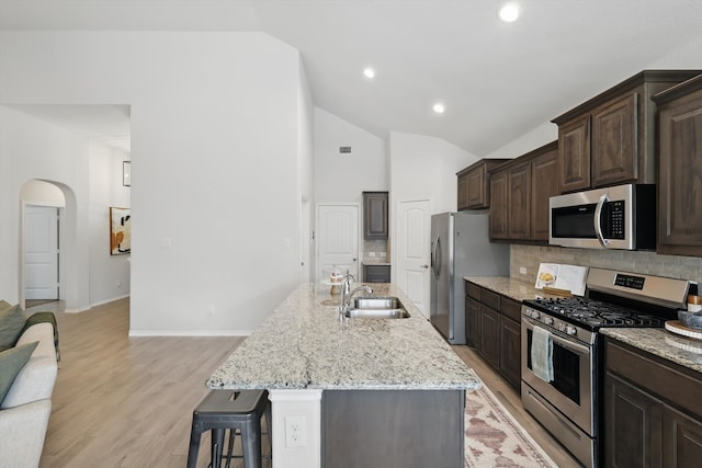 kitchen with a sink, a kitchen breakfast bar, dark brown cabinetry, stainless steel appliances, and decorative backsplash