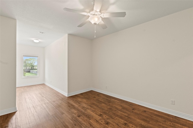 unfurnished room with dark wood-style floors, visible vents, baseboards, and a ceiling fan
