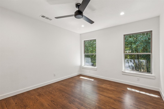 empty room featuring dark wood-style floors, a ceiling fan, visible vents, and baseboards