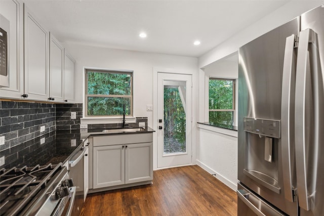 kitchen with dark wood-style flooring, a sink, tasteful backsplash, dark countertops, and appliances with stainless steel finishes