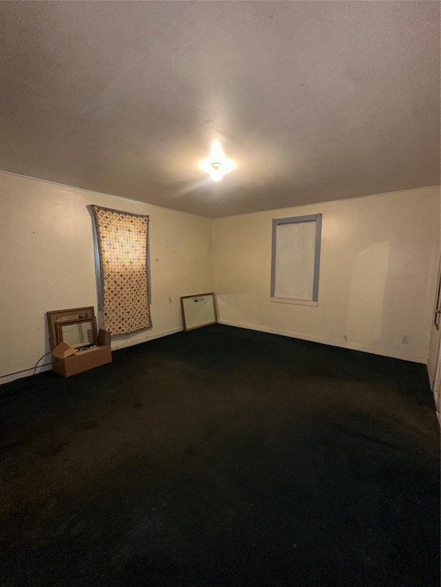 unfurnished room with baseboards and dark carpet