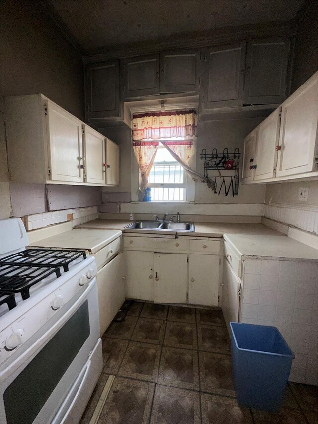 kitchen featuring light countertops, a sink, white gas range oven, and white cabinets
