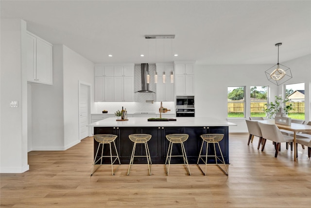 kitchen featuring stainless steel microwave, black oven, wall chimney exhaust hood, light wood-type flooring, and decorative backsplash