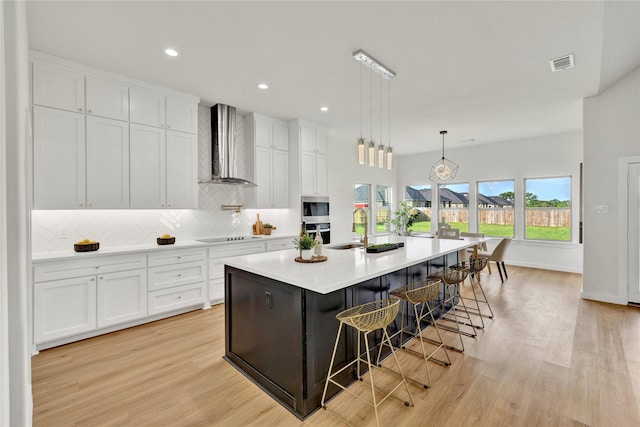 kitchen with wall chimney range hood, light wood finished floors, white cabinetry, and visible vents