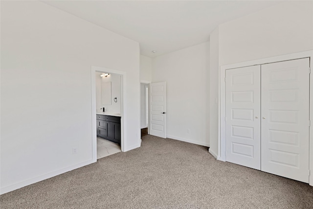 unfurnished bedroom with ensuite bath, a closet, baseboards, and light carpet