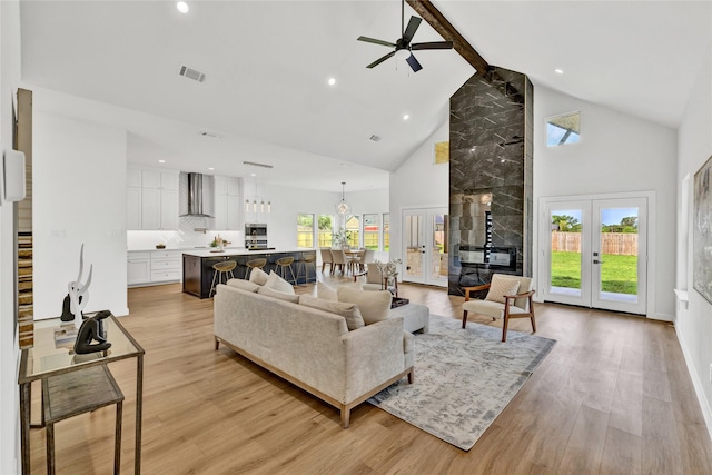 living room featuring light wood-type flooring, visible vents, beamed ceiling, ceiling fan, and high vaulted ceiling