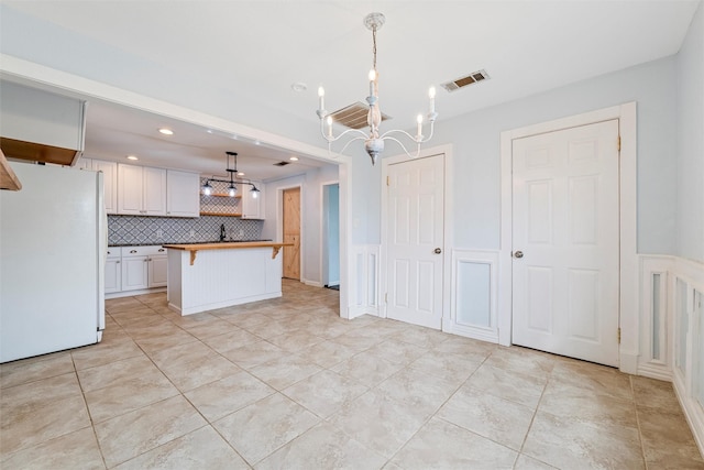 709 Verde Dr, Burleson, TX 76028 - kitchen with a chandelier, a kitchen breakfast bar, tasteful backsplash, visible vents, and freestanding refrigerator