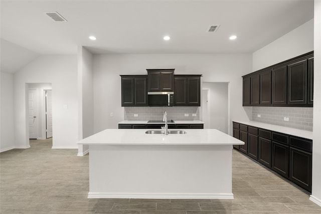 2608 Streamside Dr, Burleson, TX 76028 - kitchen with stainless steel microwave, a kitchen island with sink, decorative backsplash, light countertops, and recessed lighting