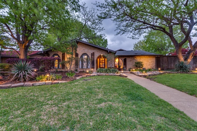 view of front of home with brick siding, fence, and a front lawn