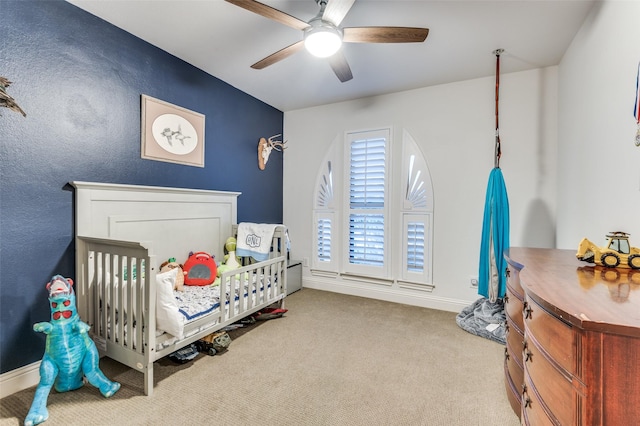 carpeted bedroom featuring a ceiling fan, a crib, and baseboards