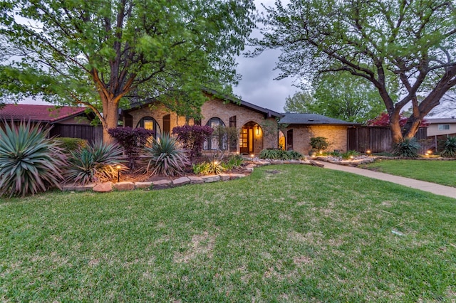 mediterranean / spanish home with brick siding, fence, and a front yard