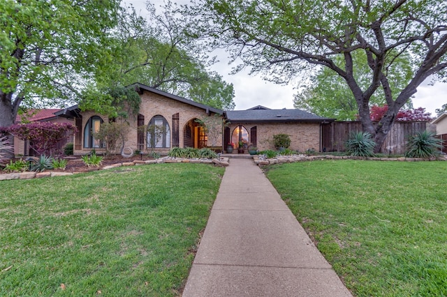 mediterranean / spanish-style home featuring brick siding, fence, and a front lawn