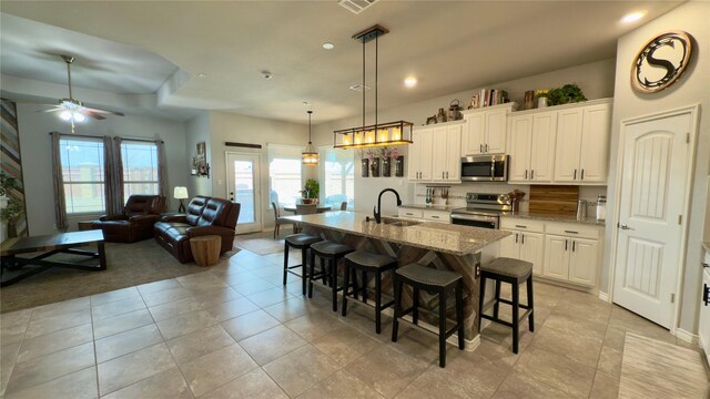 kitchen with visible vents, arched walkways, a center island with sink, a sink, and stainless steel appliances