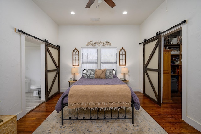bedroom with recessed lighting, ensuite bath, a barn door, and wood finished floors