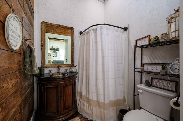 full bathroom with a textured wall, curtained shower, toilet, and vanity