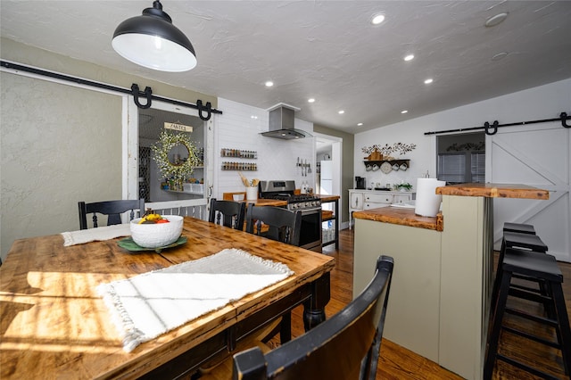 dining space with lofted ceiling, recessed lighting, a textured wall, a barn door, and wood finished floors
