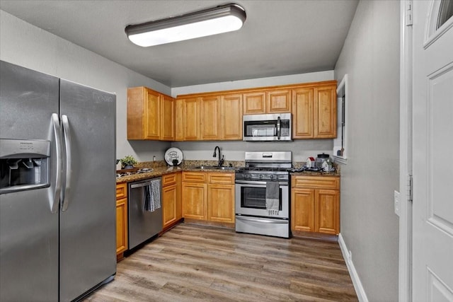 736 W Bullock Dr, Denison, TX 75020 - kitchen featuring stainless steel appliances, light wood finished floors, dark stone countertops, and a sink