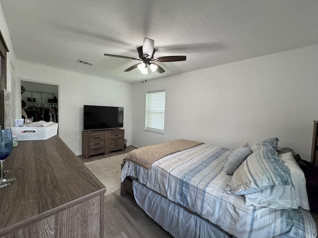 bedroom with a textured ceiling, visible vents, ceiling fan, and wood finished floors