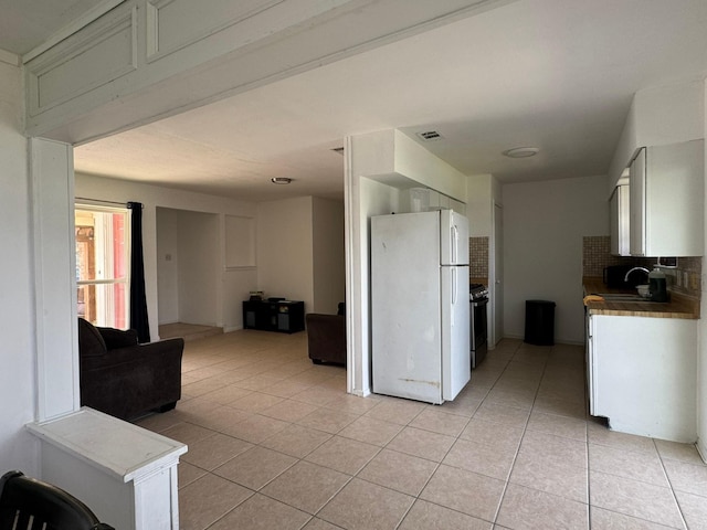kitchen with light tile patterned flooring, visible vents, tasteful backsplash, stainless steel gas range oven, and freestanding refrigerator