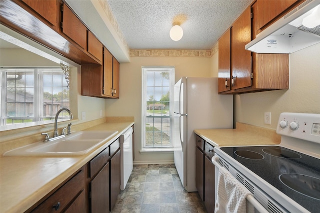 5912 Oregon Trl Ct, Haltom City, TX 76148 - kitchen with light countertops, white appliances, under cabinet range hood, a sink, and brown cabinetry
