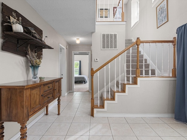 stairway with a textured ceiling, tile patterned floors, visible vents, and baseboards