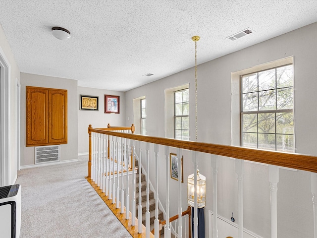 hallway featuring light colored carpet, a textured ceiling, baseboards, an upstairs landing, and visible vents