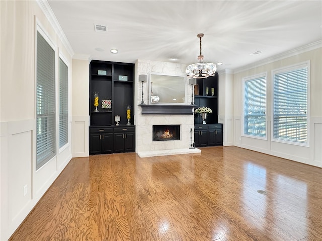 unfurnished living room featuring built in shelves, a decorative wall, crown molding, and visible vents