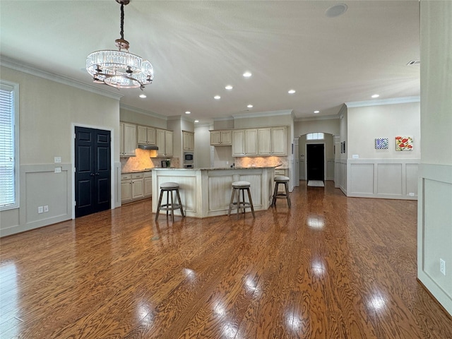 kitchen with arched walkways, an inviting chandelier, a kitchen bar, wood finished floors, and a decorative wall