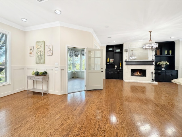 unfurnished living room with plenty of natural light, wood finished floors, a large fireplace, and ornamental molding