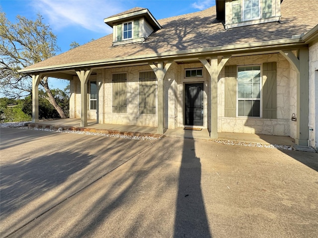 view of front of home with stone siding, a shingled roof, and covered porch