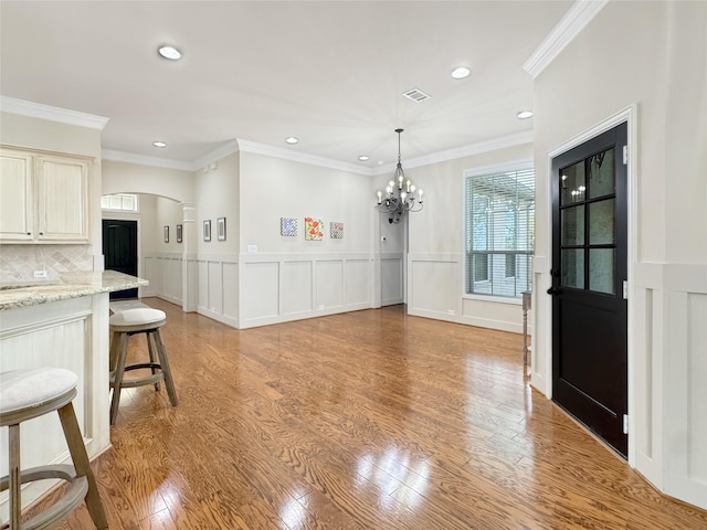 dining space with arched walkways, light wood-type flooring, and an inviting chandelier